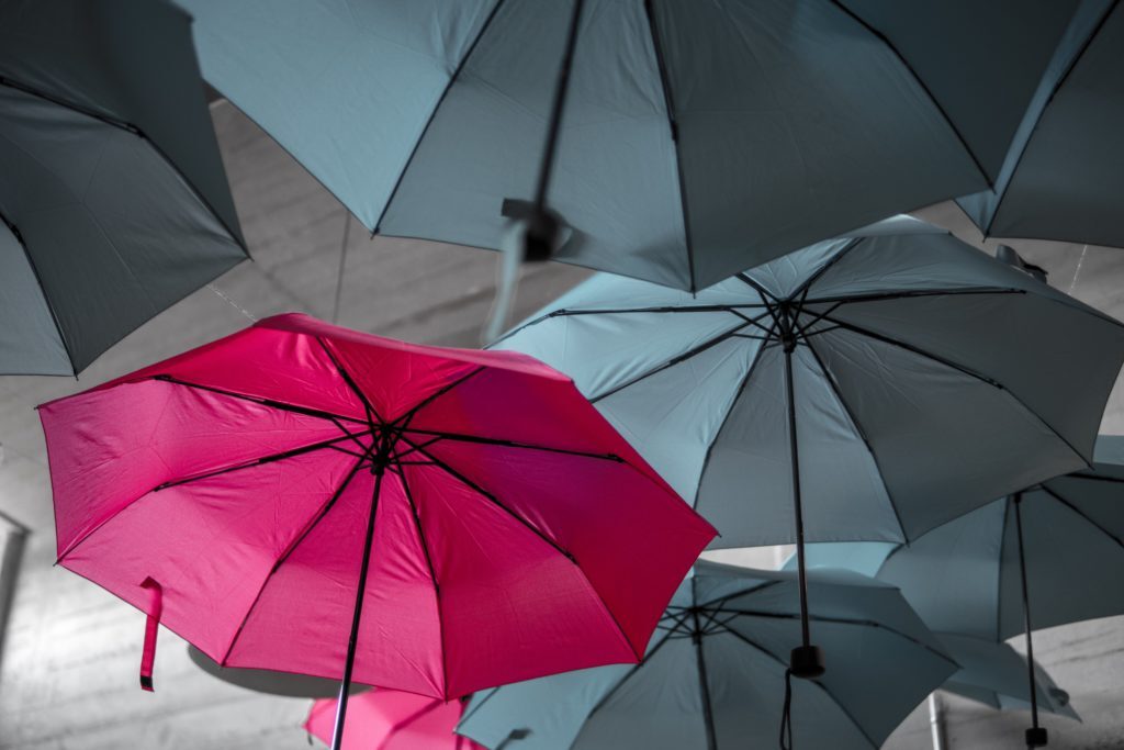 One red umbrella among many grey ones